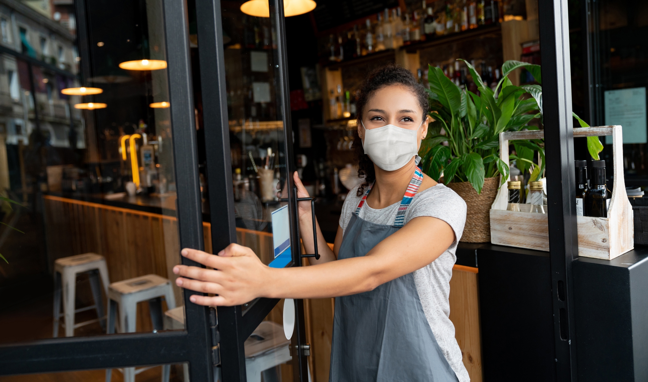 mulher de máscara abrindo porta de restaurante