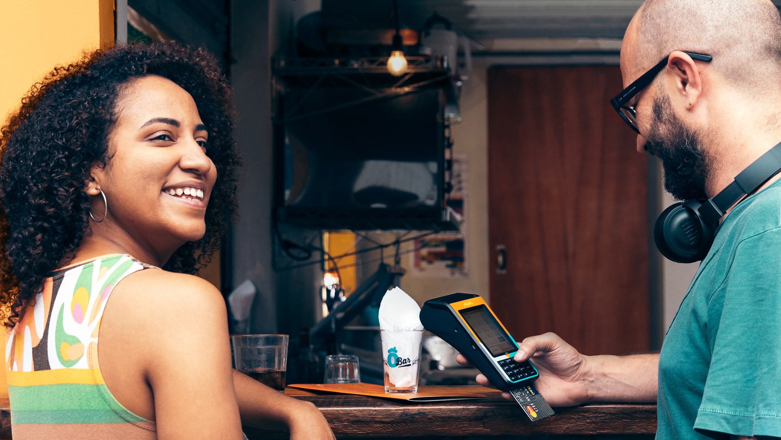 Mulher sorrindo ao lado de um homem com pagando em uma maquininha de cartão rede